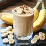 A creamy peanut butter banana smoothie in a glass, topped with banana slices and a drizzle of peanut butter.